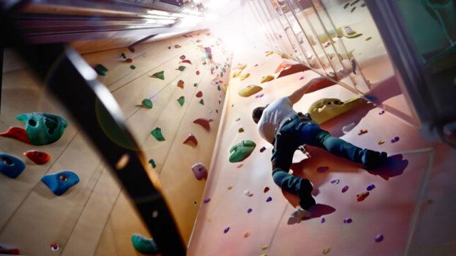 A rock climber going up a rock-climbing wall repurposed from an empty elevator shaft